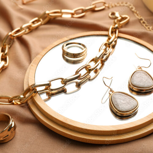 Stylish golden bijouterie and mirror on light brown fabric, closeup